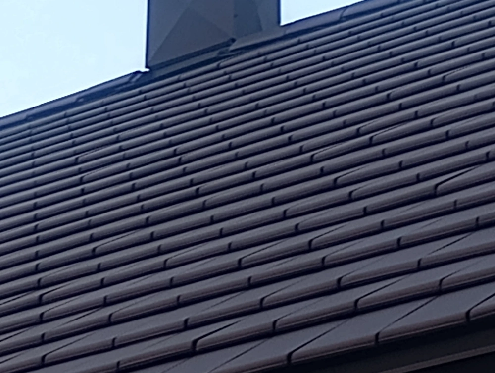 Pokrycie dachowe z brązowych dachówek ceramicznych na dwuspadowym dachu z kominem