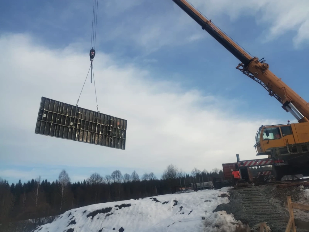 Dźwig podnosi szalunek ścienny na zaśnieżonym terenie budowy, Roboty żelbetowe