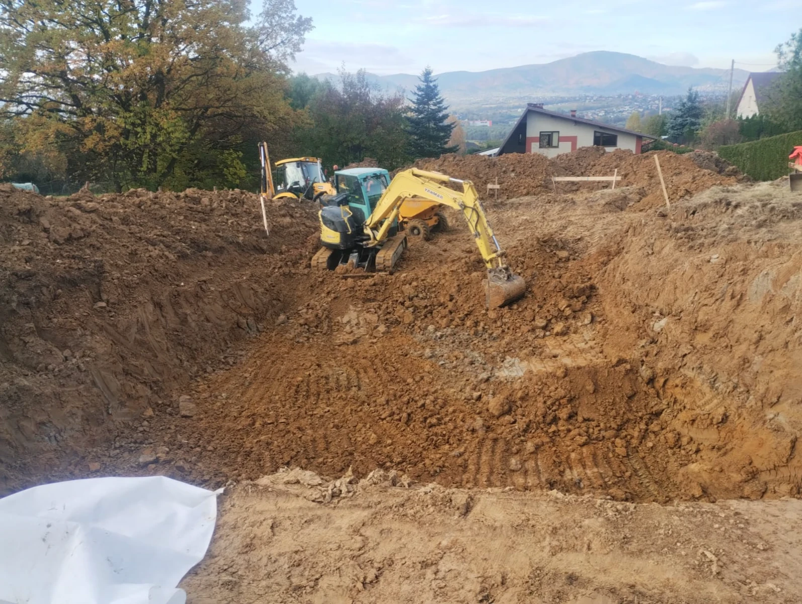 Koparka wykonująca prace ziemne pod fundamenty domu, widoczny wykop i niwelacja terenu
